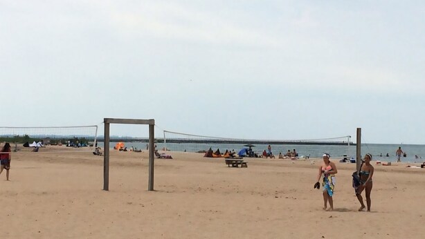 Ein Beachvolleyballfeld mit Netz, Zelten und Personen im Hintergrund.