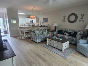 A living room with a sofa, coffee table, and a dining area with chairs and a kitchen in the background. - Arcadian Shores 2BR/2BA Condo Sleeps 6 • Pool • Balcony • Near Beach (Myrtle Beach)