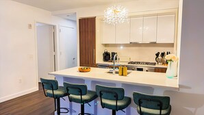 Une cuisine moderne avec des meubles blancs, un îlot central doté de tabourets, un lustre et une cuisinière.