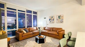 A modern living room with a leather sectional sofa, a black coffee table, and a city view through large windows. - Luxury Midtown West High Rise with Skyline Views (New York)