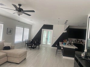 Ein modernes Wohnzimmer mit einer Couch, einem Esstisch und Stühlen, eine Küche mit Fernseher und eine Treppe, die zu einer weiteren Ebene führt.