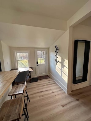 Ein Zimmer mit einem Holzesstisch, zwei Stühlen, einer weißen Tür und einem Spiegel mit schwarzem Rahmen.