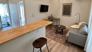 Ein zeitgemäßer Wohnraum mit Holzboden, einem Flachbildfernseher, einer Couch und einem kleinen Tisch.