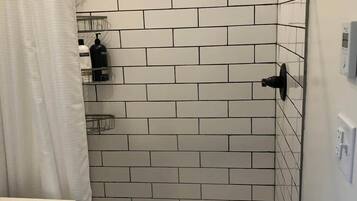 A bathroom with white subway tiles, a shower with a black rain showerhead, a white curtain, and a wall-mounted soap dispenser.