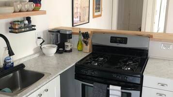 Et køkken med komfur, vask og diverse køkkenredskaber. Der er hylder med service og en kaffemaskine.