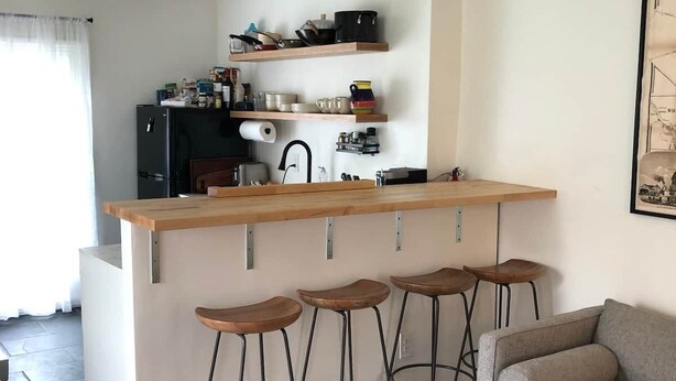 Ett kompakt vardagsrum med ett litet kök, en soffa, ett soffbord och en mönstrad matta.