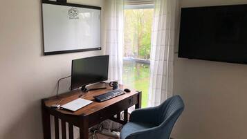 Una habitación con escritorio, computadora, silla, televisor y ventana con cortinas.
