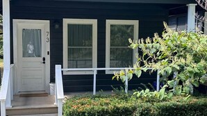 A dark-colored single-story house with a front porch, two windows, and a door.