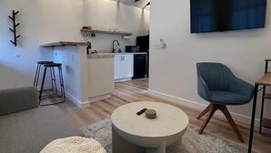 A modern living room with a round coffee table, a blue armchair, and a kitchen in the background.
