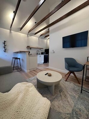 Una sala moderna con una mesita de centro redonda, un sillón azul y una cocina al fondo.