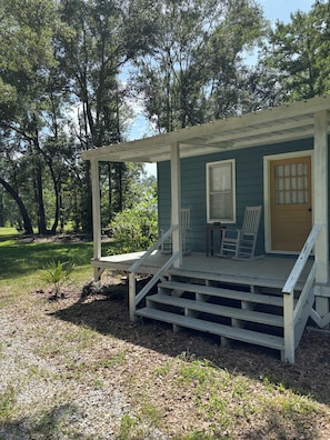 A wooden porch with steps leading to a door, two rocking chairs, and a covered area with a window.