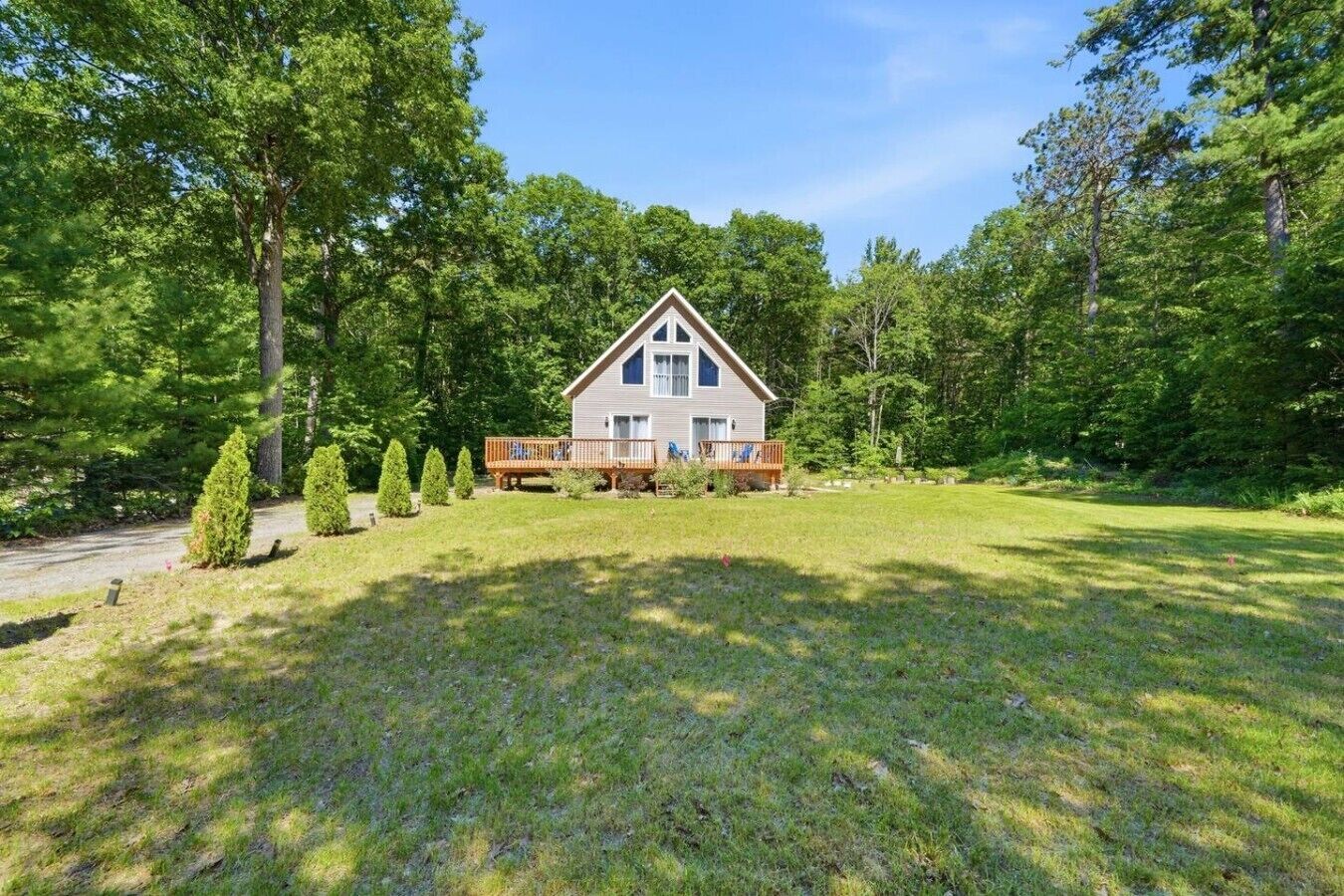 A two-story house with a deck, surrounded by a well-maintained lawn and tall trees.