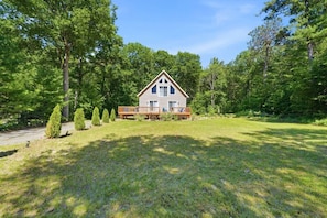A two-story house with a deck, surrounded by a well-maintained lawn and tall trees.