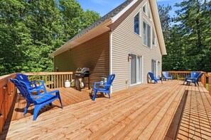 A wooden deck with blue chairs, a grill, and a house with a sloped roof.