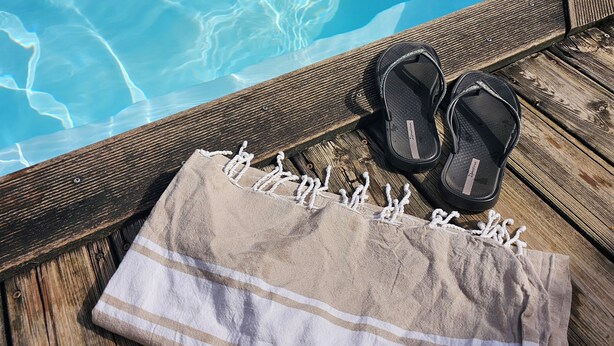 Eine Holzterrasse mit Pool, einem Handtuch und einem Paar Sandalen.