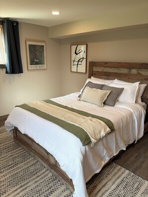 A neatly made bed with a wooden headboard, a patterned rug, and two framed artworks on the wall. - Cozy Foothills Escape w/ Mountain Views  | Near Calgary & Banff (Rural Rocky View County)