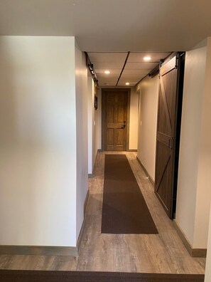 A hallway with a wooden door at the end, a dark carpet, and a light-colored wall. - Cozy Foothills Escape w/ Mountain Views  | Near Calgary & Banff (Rural Rocky View County)