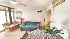 A living room with a green sofa, a wooden chair, a table with a patterned tablecloth, a potted plant, and a wall-mounted air conditioner. - Stunning apartment with a pool near the large beach at Le Diamant (Le Diamant)