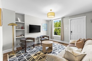 Un salon moderne avec un téléviseur à écran plat, deux fauteuils, une table basse ronde et un tapis à motifs.