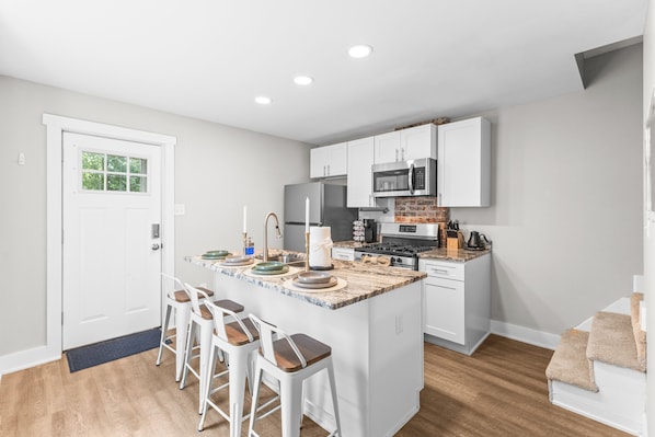 A modern kitchen with white cabinets, a central island with stools, a refrigerator, microwave, and stove.