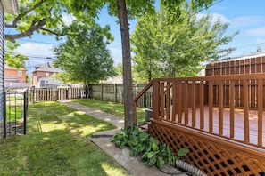 A backyard with a wooden deck, a tree, and a fence.