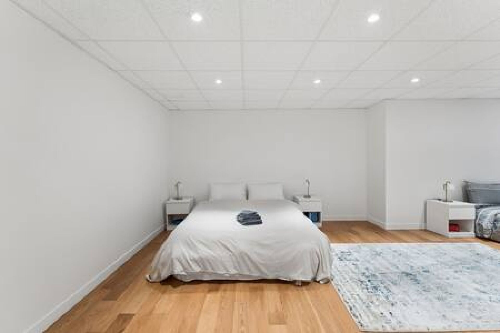 A bedroom with a bed, bedside tables, a nightstand, a rug, and a wall-mounted light fixture.