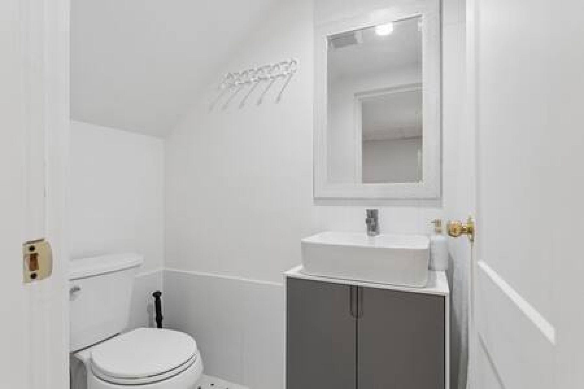 Une petite salle de bain blanche, avec des toilettes, un lavabo et un miroir au-dessus.