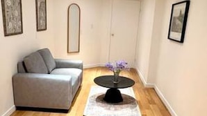 Et værelse med en grå sofa, et rundt bord med en vase, trægulv og billeder i rammer på væggene.