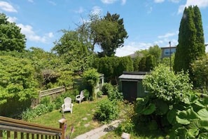 Ein Garten mit einer Holzdielen-Terrasse, einem Schuppen und einem hohen Baum.