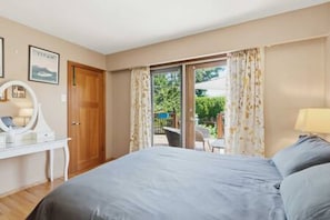 A bedroom with a bed, a desk, a chair, and a view of the outdoors.