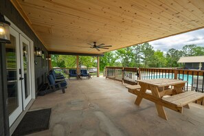 Eine überdachte Terrasse mit Holzmöbeln, einem Deckenventilator und Blick auf einen Swimmingpool.