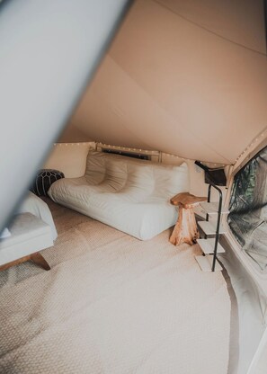 Ein Zeltraum mit einer weißen Couch, einem kleinen Holzschemel und einer schwarzen Lampe.