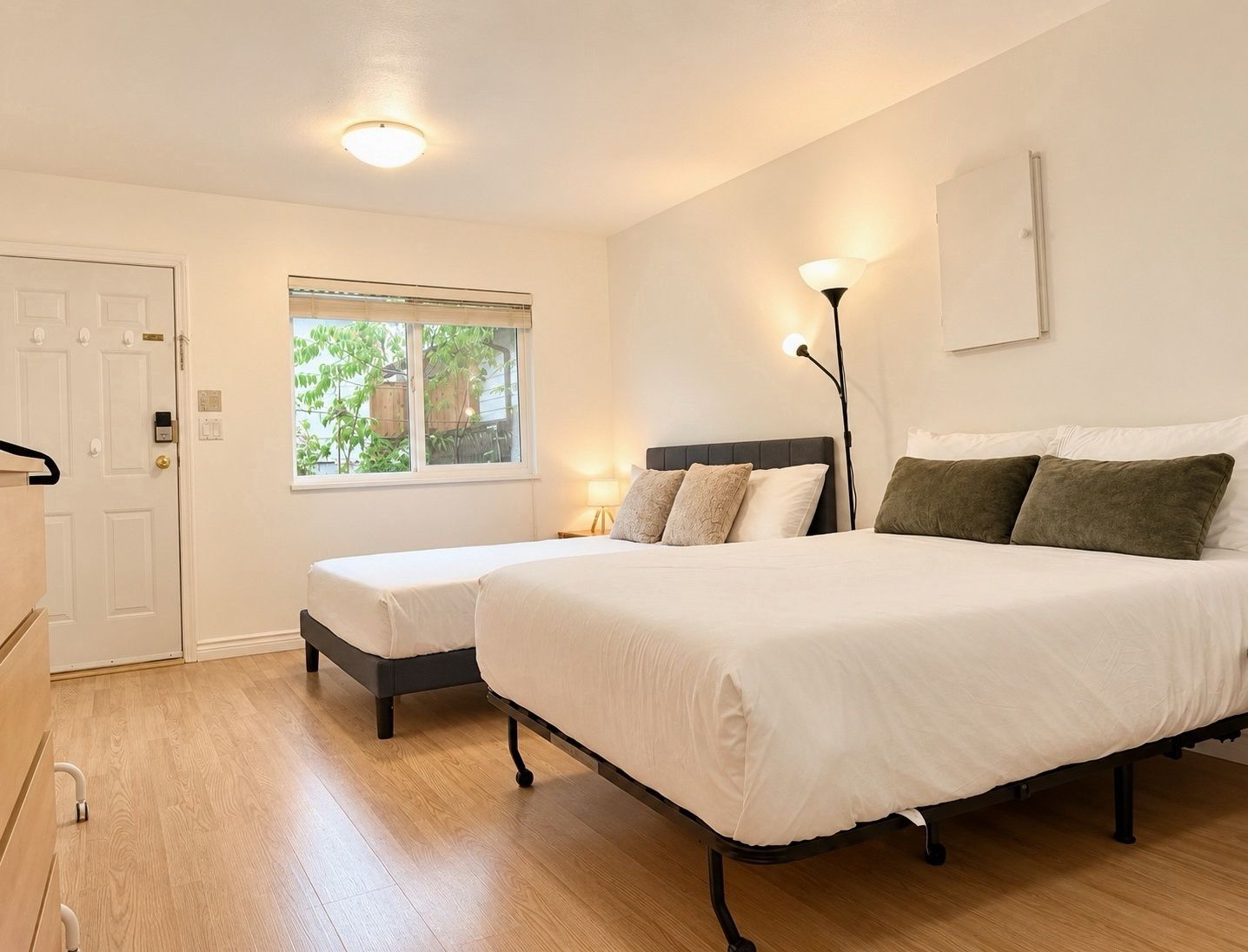 Een slaapkamer met twee bedden, een raam, een deur en een bedlampje.