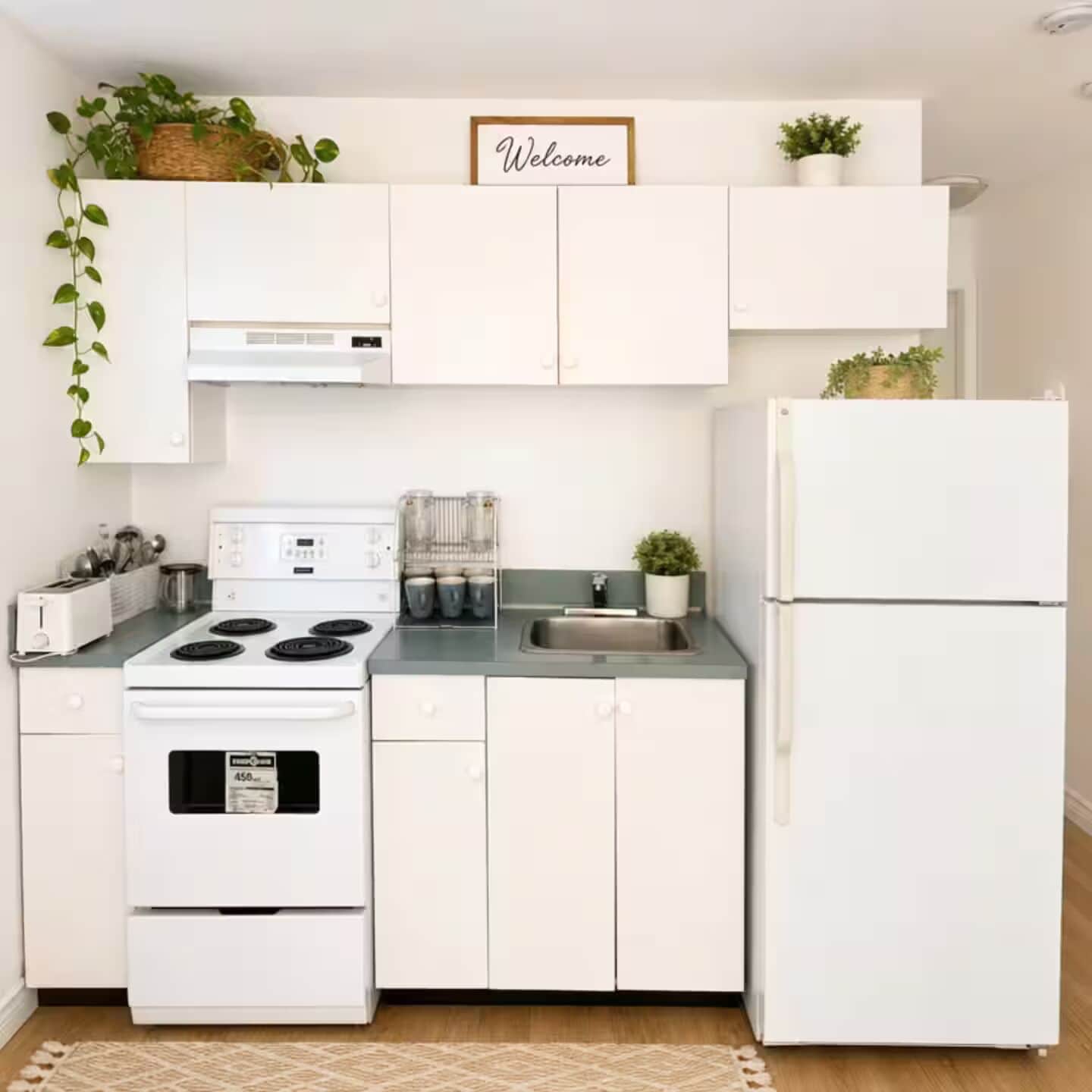 Une cuisine avec des meubles blancs, une cuisinière, un réfrigérateur et un panneau d’accueil placé au-dessus des meubles.