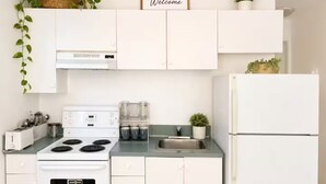 Een keuken met witte kastjes, een fornuis, een koelkast en een welkomstbord boven de kastjes.