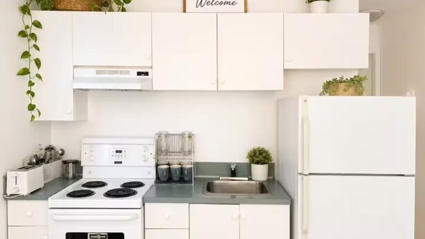 A kitchen with white cabinets, a stove, a refrigerator, and a welcome sign above the cabinets.