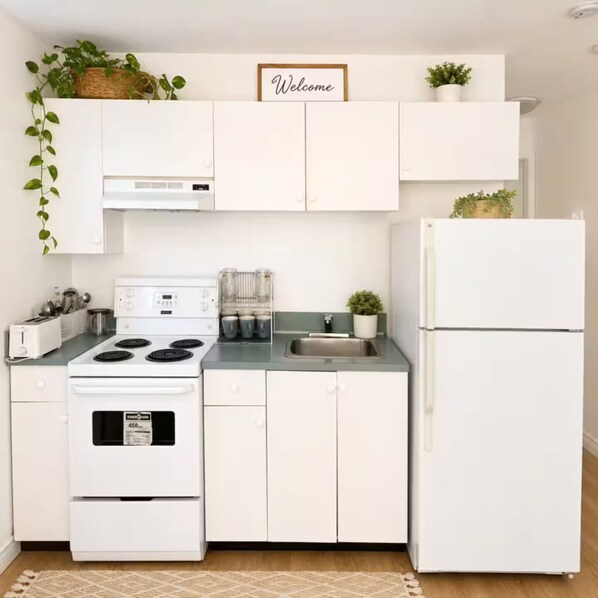 A kitchen with white cabinets, a stove, a refrigerator, and a welcome sign above the cabinets. - Studio in Sophia’s sweet home (Vancouver)