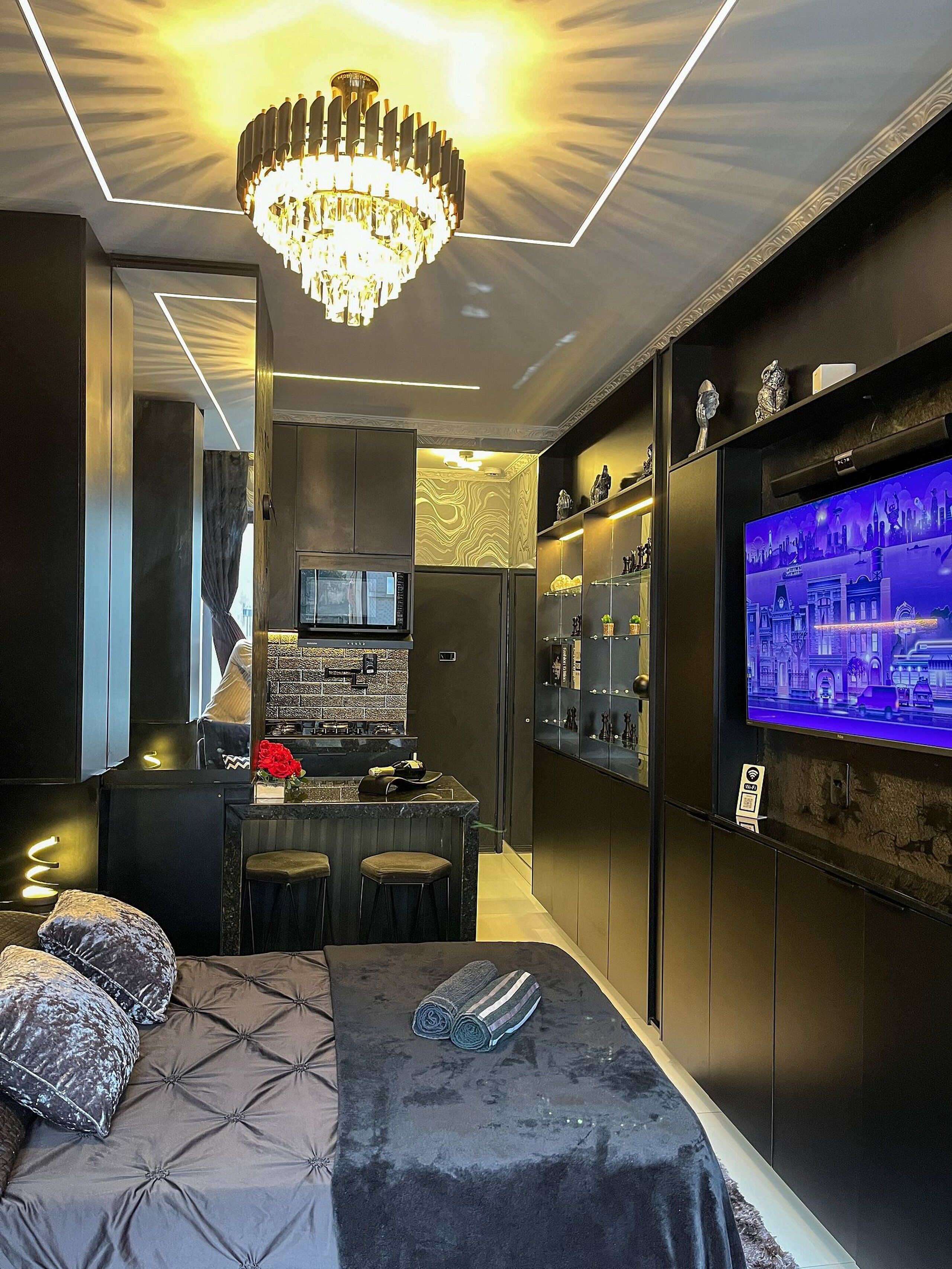 Ein modernes Hotelzimmer mit einem großen Bett, einem Fernseher, einer Minibar und einem Chandelier.