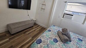 A bedroom with a bed, a bench, a TV, a small table, and a window. - Cozy & Central 1-Bedroom | Near the Design District (Miami)