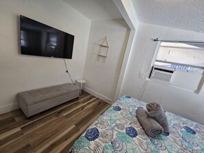 Een slaapkamer met een bed, een bankje, een televisie, een klein tafeltje en een raam.