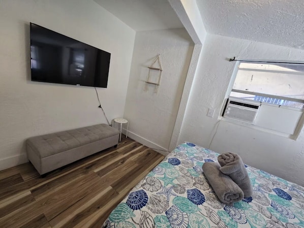 Ein Schlafzimmer mit Bett, einer Sitzbank, einem Fernseher, einem kleinen Tisch und einem Fenster.