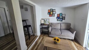 A living room with a grey sofa, a coffee table with sunflowers, a black chair, and a small side table. - Cozy & Central 1-Bedroom | Near the Design District (Miami)