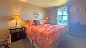 A bedroom with a bed, two bedside tables with lamps, a decorative wall piece, a window with a view, and a dresser. - Oceanfront Suite with Relaxing Tub & Private Bath - Rm 5 (Gabriola)
