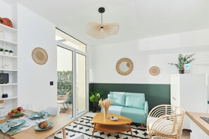 Ein modernes Wohnzimmer mit einer Couch, einem Couchtisch und Korbstühlen. Regale mit Dekorationselementen und ein Fernseher sind ebenfalls vorhanden.