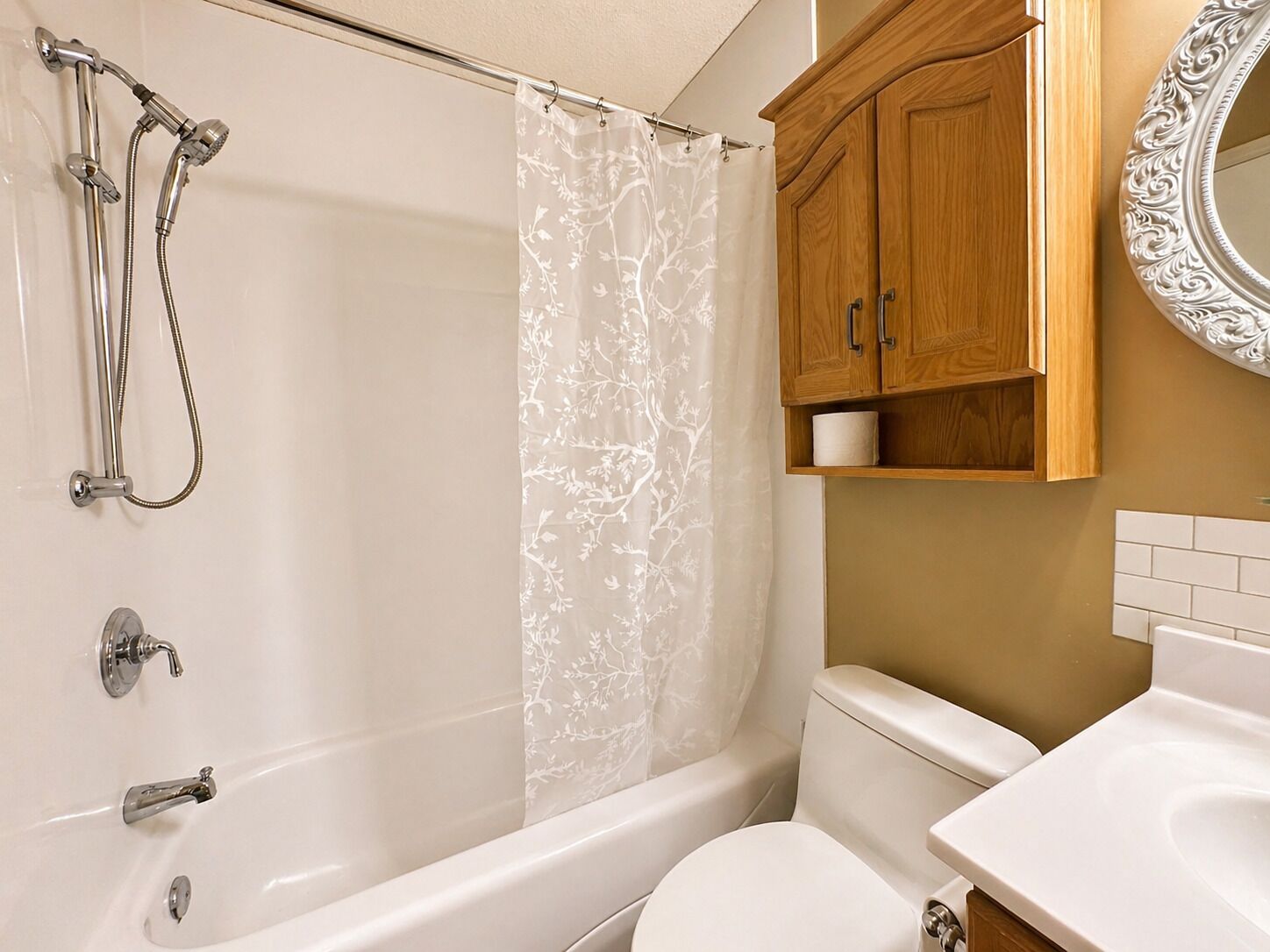 Un baño con bañera, ducha, inodoro, armario de madera y un espejo.
