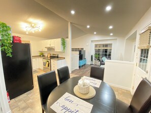 A modern kitchen with white cabinets, a black refrigerator, and a dining area with a table set for two. - Across road to Nose Creek Park Cozy city hideaway for family 3BD 2BA/Fenced yard (Calgary)