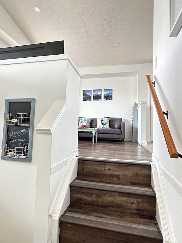 Eine Treppe führt zu einem Wohnbereich mit einer Couch, einem Couchtisch und Wandbildern.