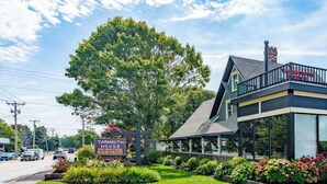 A Yarmouth House with a signboard, a grassy lawn, and a building with a balcony. - Cozy Cape Cod 17A with Fire Pit Near Beaches (Yarmouth)
