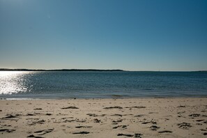 Ein Strand mit Fußspuren, die zum Wasser führen, ein klarer Himmel und eine entfernte Küste.