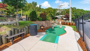A miniature golf course with a green putting surface, wooden benches, and a chain-link fence. - Cozy Cape Cod 17A with Fire Pit Near Beaches (Yarmouth)